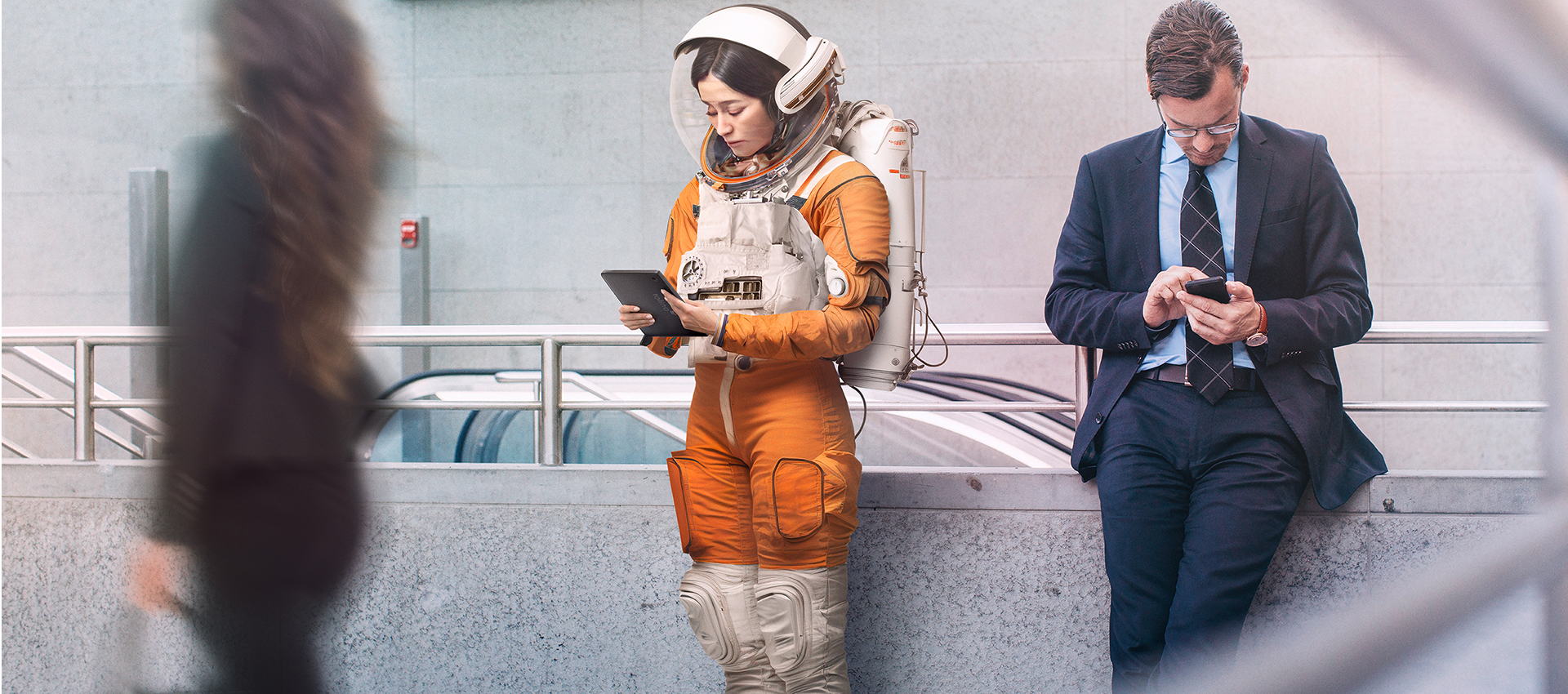 Astronautin mit tolino eReader liest neben wartendem Mann am Bahnsteig
